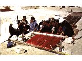 A family helping to weave at a home-constructed loom.